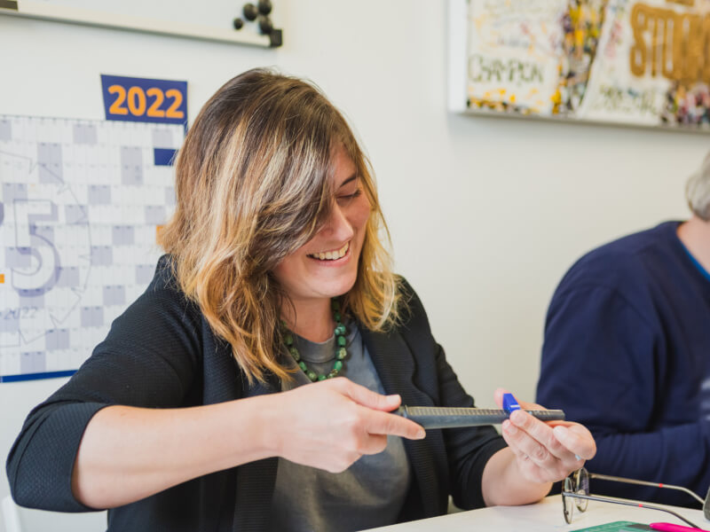 A smiling woman sits at a work station, sizing a blue ring blank at a jewellery workshop